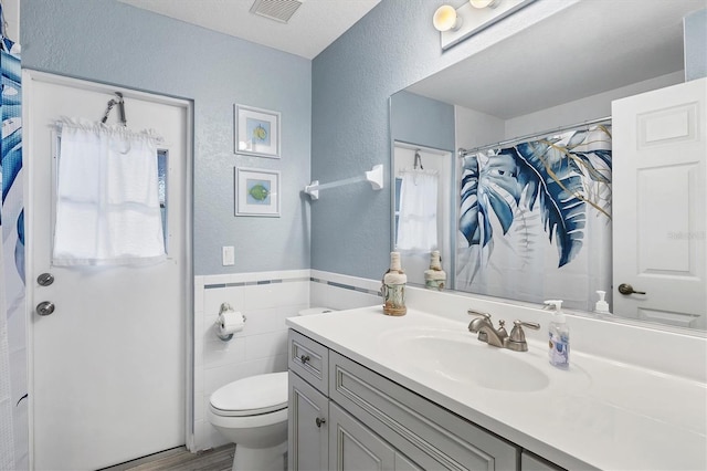 bathroom with toilet, tile walls, vanity, and walk in shower