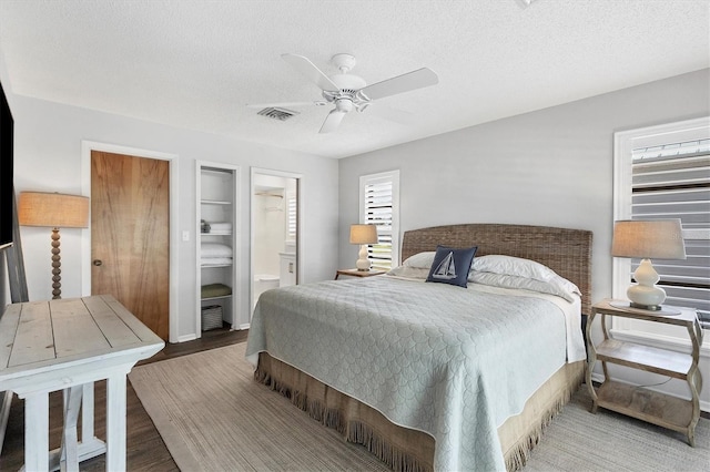 bedroom featuring ceiling fan, connected bathroom, a textured ceiling, and hardwood / wood-style flooring