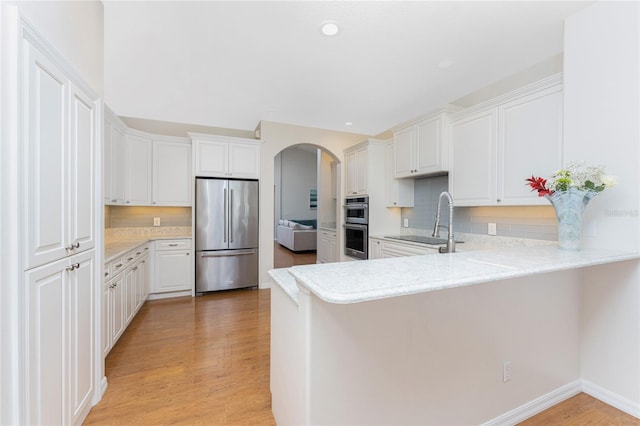 kitchen with white cabinets, light hardwood / wood-style floors, kitchen peninsula, and stainless steel appliances