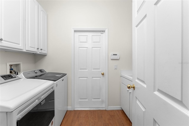 laundry room featuring washer and dryer, light wood-type flooring, and cabinets