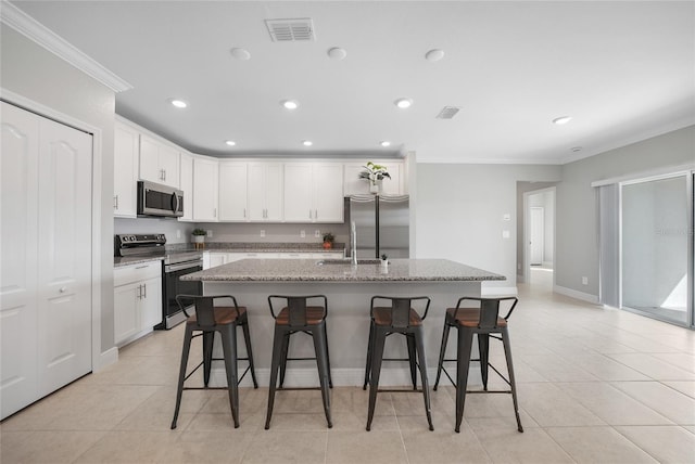 kitchen with a kitchen bar, stainless steel appliances, light stone counters, and an island with sink