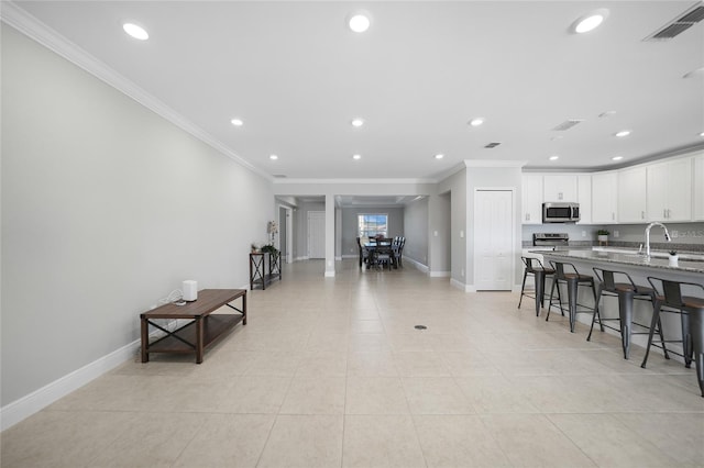 kitchen featuring a breakfast bar area, stone counters, white cabinetry, and crown molding