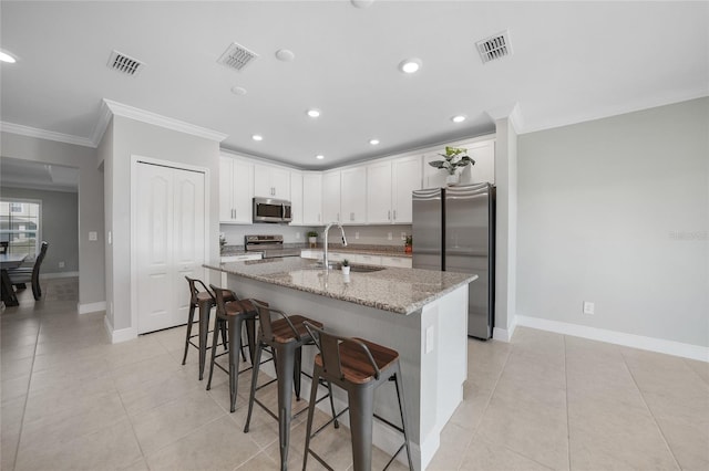 kitchen with sink, light stone counters, a breakfast bar, white cabinets, and appliances with stainless steel finishes