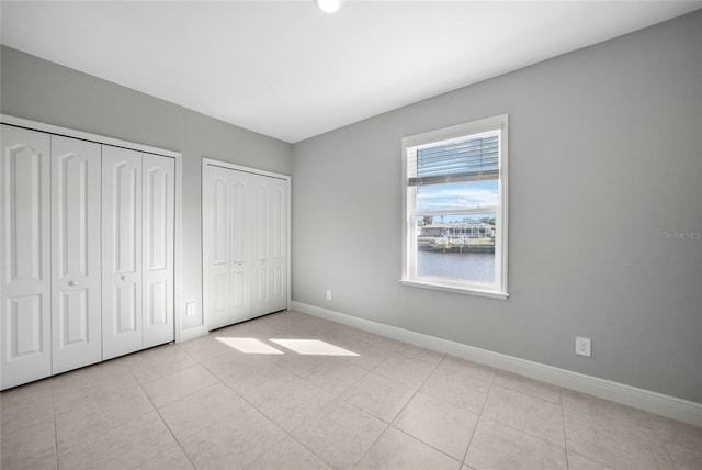 unfurnished bedroom with light tile patterned flooring, two closets, and a water view