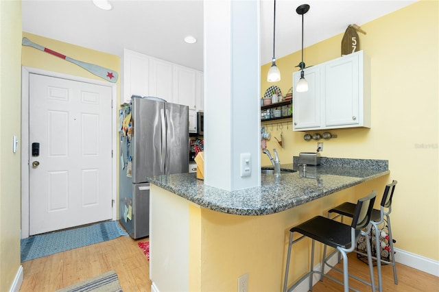 kitchen with light hardwood / wood-style flooring, kitchen peninsula, stainless steel fridge, a kitchen bar, and white cabinets