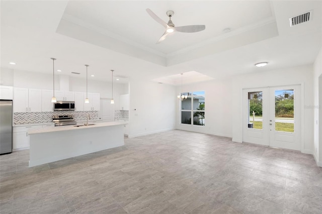 kitchen with a tray ceiling, hanging light fixtures, appliances with stainless steel finishes, and an island with sink