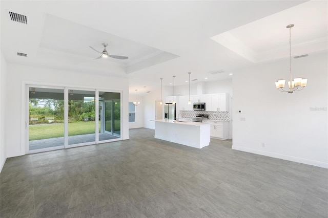 unfurnished living room featuring a raised ceiling, sink, and ceiling fan with notable chandelier