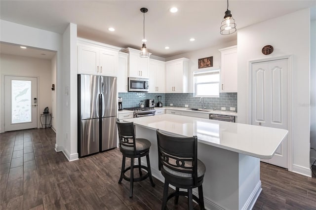 kitchen with appliances with stainless steel finishes, pendant lighting, white cabinets, dark hardwood / wood-style floors, and a kitchen island