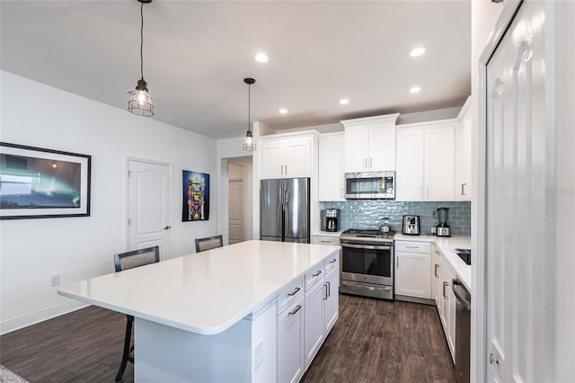 kitchen featuring appliances with stainless steel finishes, dark hardwood / wood-style flooring, decorative light fixtures, white cabinets, and a center island