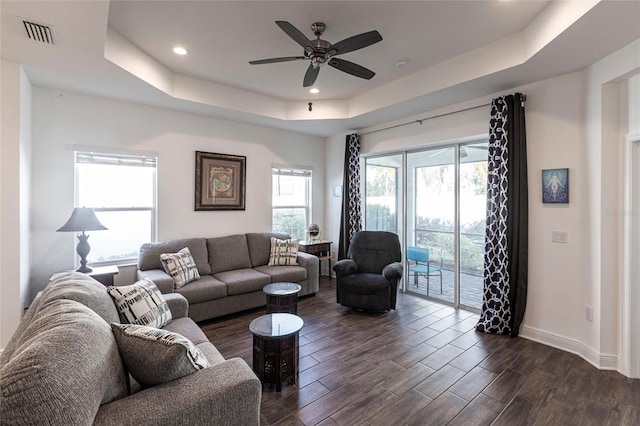 living room featuring a tray ceiling, a healthy amount of sunlight, and dark hardwood / wood-style floors