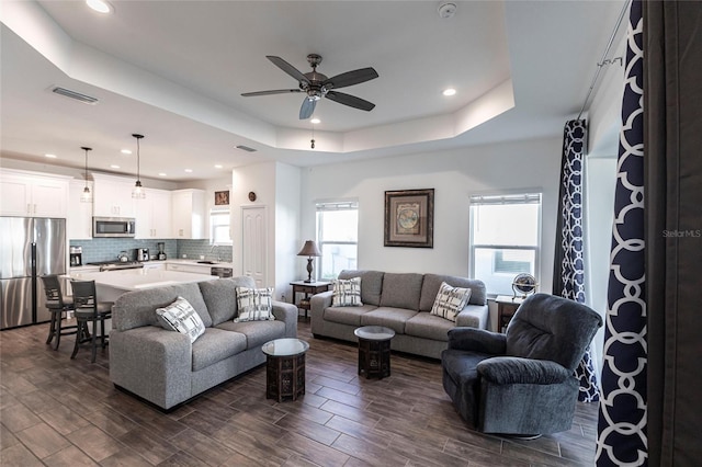 living room featuring a healthy amount of sunlight, a tray ceiling, ceiling fan, and dark wood-type flooring