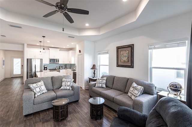 living room featuring a tray ceiling, ceiling fan, sink, and dark hardwood / wood-style floors