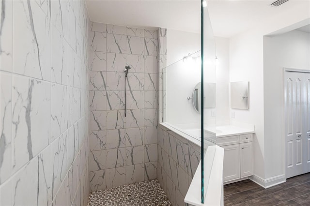 bathroom with hardwood / wood-style floors, vanity, and a tile shower