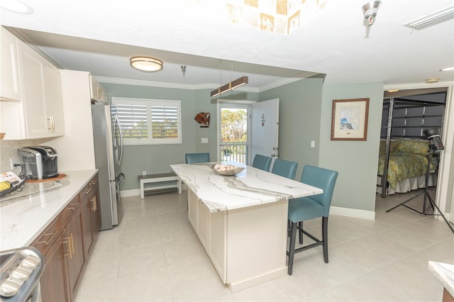 kitchen featuring a breakfast bar, ornamental molding, a kitchen island, light stone counters, and stainless steel refrigerator