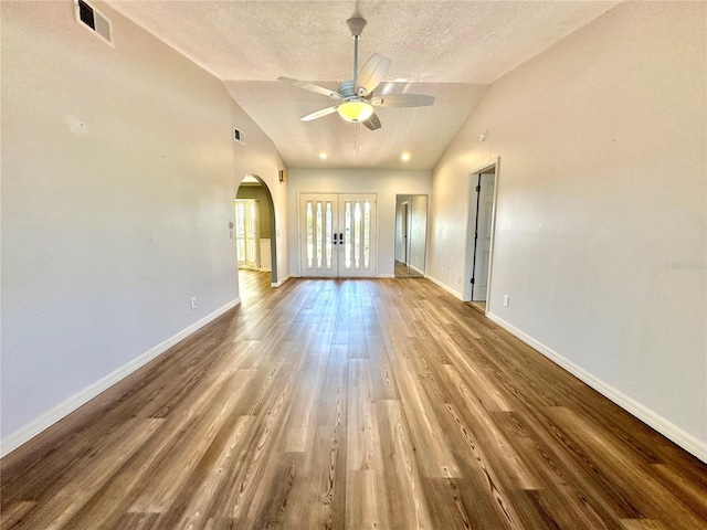 unfurnished living room with french doors, a textured ceiling, vaulted ceiling, ceiling fan, and hardwood / wood-style floors