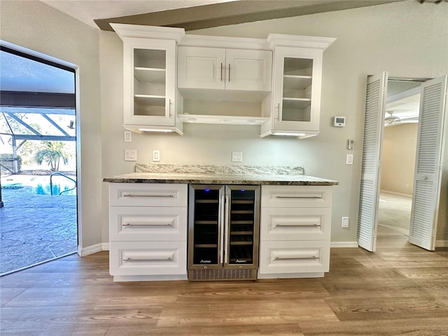 bar featuring white cabinets, light stone countertops, wine cooler, and light hardwood / wood-style flooring