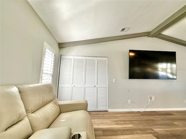 living room with hardwood / wood-style floors, vaulted ceiling with beams, and a textured ceiling