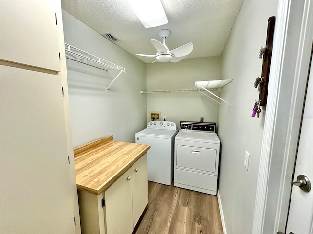 washroom with cabinets, a textured ceiling, ceiling fan, light hardwood / wood-style flooring, and washing machine and dryer