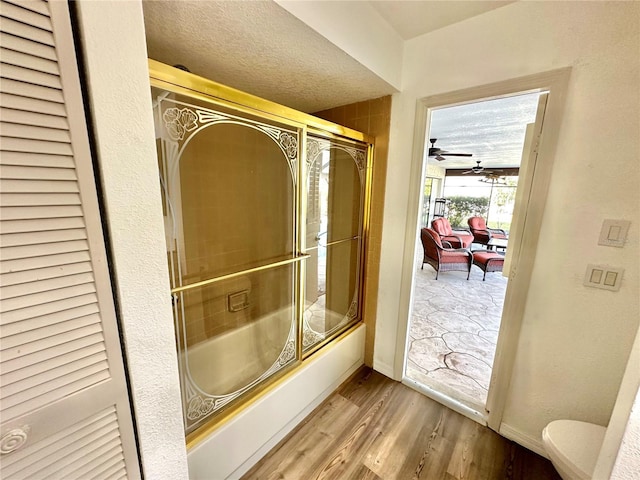 bathroom featuring ceiling fan, hardwood / wood-style floors, a textured ceiling, toilet, and shower / bath combination with glass door