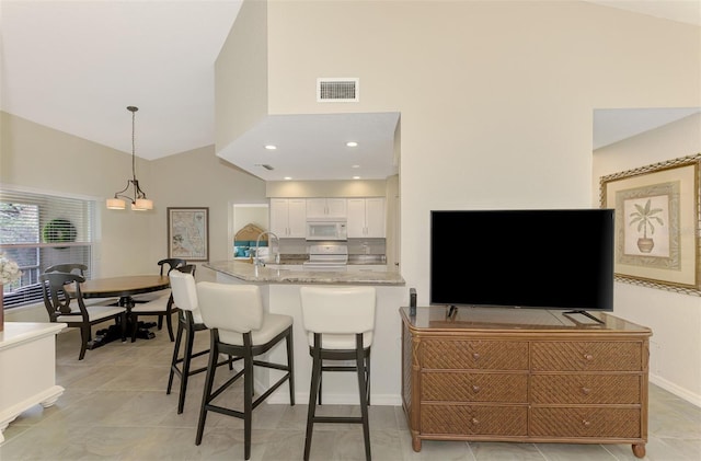 kitchen featuring light stone countertops, a breakfast bar, sink, pendant lighting, and white cabinetry