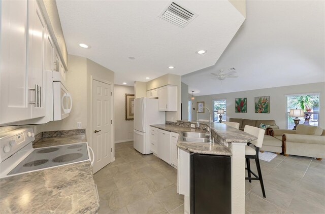 kitchen with a kitchen bar, light stone countertops, white appliances, sink, and white cabinetry