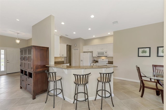 kitchen featuring light stone countertops, kitchen peninsula, white appliances, a breakfast bar area, and white cabinets