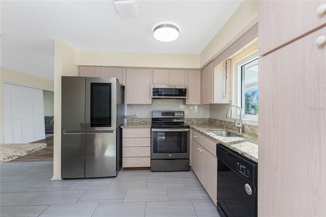 kitchen with stainless steel appliances, backsplash, light brown cabinetry, a sink, and light stone countertops