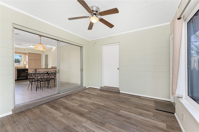 empty room with baseboards, wood finished floors, a ceiling fan, and crown molding