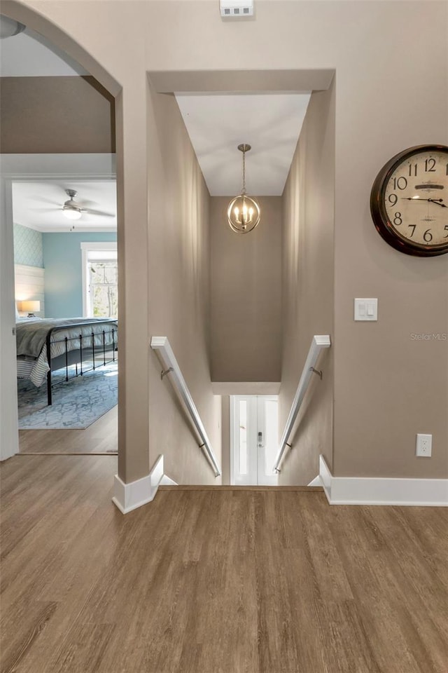 stairs with a chandelier, wood finished floors, and baseboards