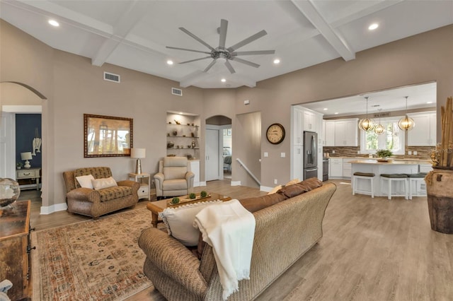 living area with light wood-type flooring, arched walkways, visible vents, and coffered ceiling