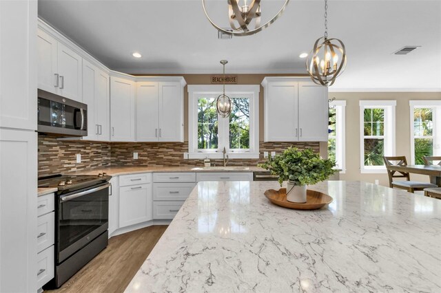 kitchen featuring decorative light fixtures, appliances with stainless steel finishes, white cabinetry, a sink, and a chandelier