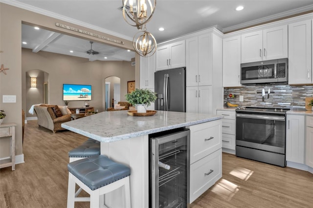 kitchen with arched walkways, beverage cooler, stainless steel appliances, white cabinets, and open floor plan