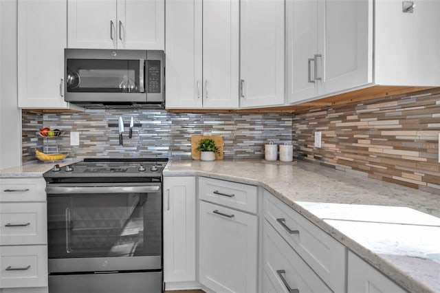 kitchen with tasteful backsplash, appliances with stainless steel finishes, white cabinets, and light stone counters