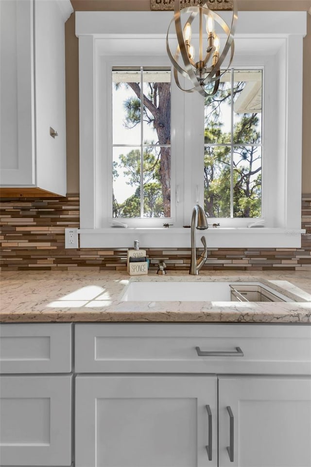 kitchen featuring a notable chandelier, a sink, white cabinetry, light stone countertops, and tasteful backsplash