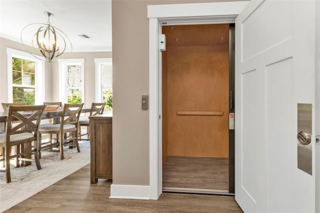 interior space with visible vents, an inviting chandelier, ornamental molding, elevator, and wood finished floors