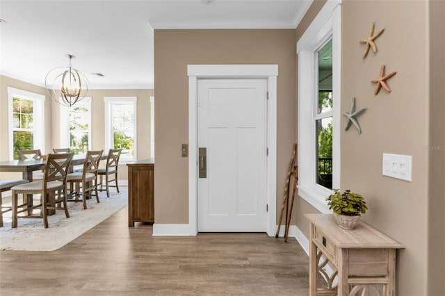 foyer featuring a notable chandelier, crown molding, baseboards, and wood finished floors