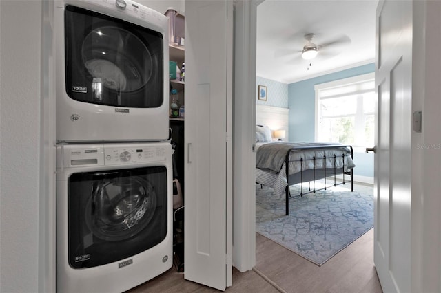 clothes washing area featuring crown molding, a ceiling fan, stacked washing maching and dryer, wood finished floors, and laundry area