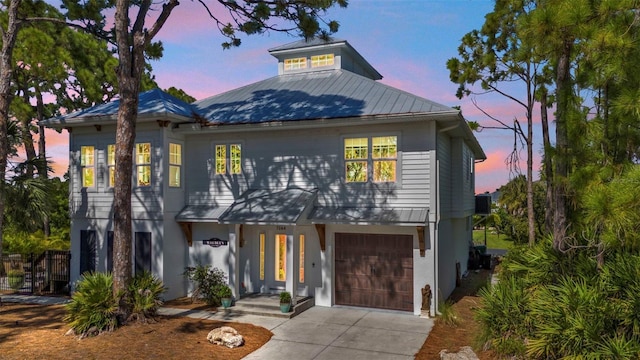 coastal inspired home with driveway, an attached garage, and metal roof