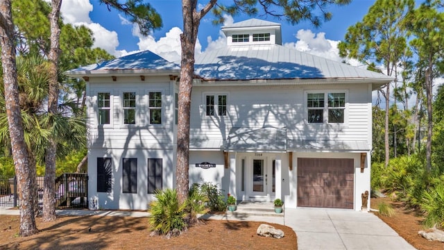 coastal home featuring a garage, concrete driveway, metal roof, and fence