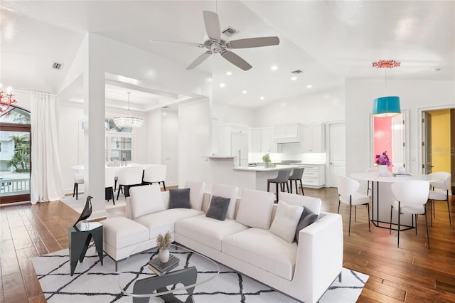 living room with ceiling fan with notable chandelier, dark wood-type flooring, and vaulted ceiling