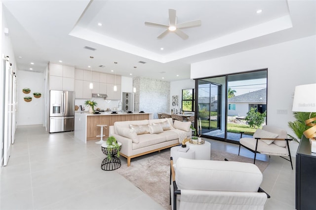 tiled living room with ceiling fan and a raised ceiling