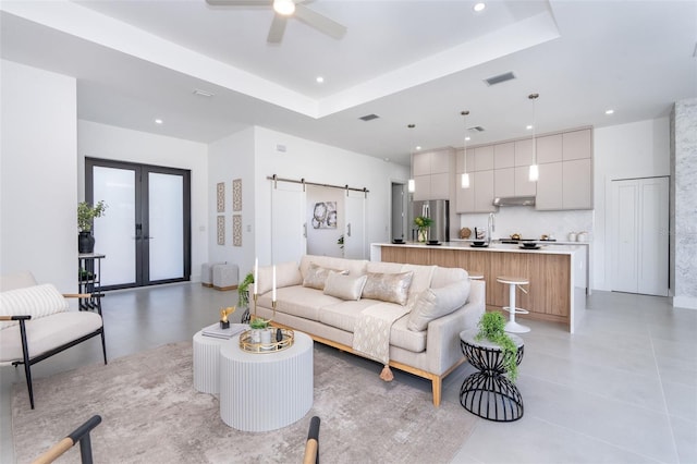 living room featuring french doors, a raised ceiling, ceiling fan, light tile patterned floors, and a barn door