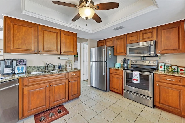 kitchen featuring light stone counters, stainless steel appliances, a raised ceiling, sink, and light tile patterned flooring