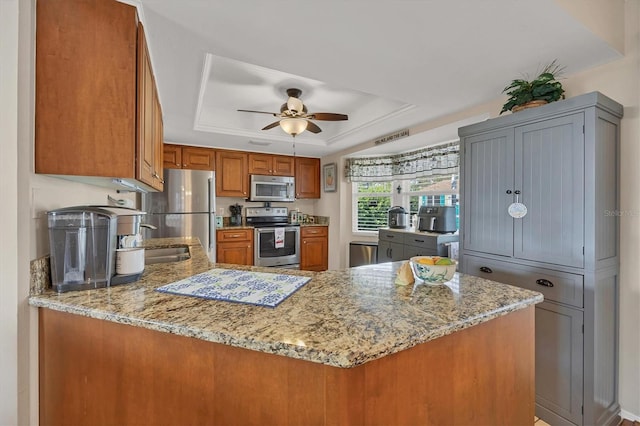 kitchen with light stone countertops, kitchen peninsula, appliances with stainless steel finishes, and a tray ceiling