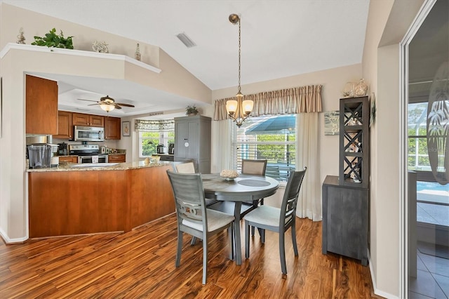 dining space with ceiling fan with notable chandelier, a raised ceiling, dark hardwood / wood-style flooring, and vaulted ceiling