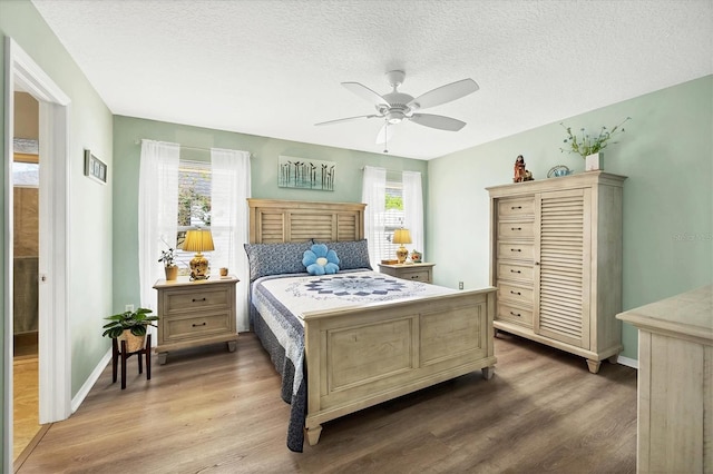 bedroom with multiple windows, ceiling fan, a textured ceiling, and hardwood / wood-style flooring