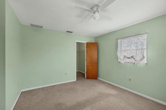 unfurnished bedroom with ceiling fan, a textured ceiling, a walk in closet, light carpet, and a closet