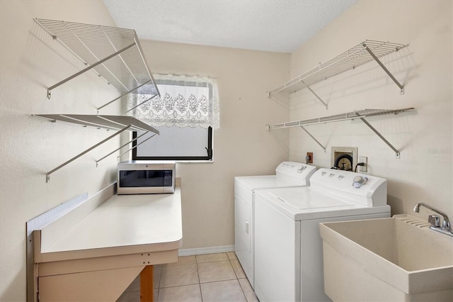 clothes washing area featuring washing machine and clothes dryer, sink, light tile patterned flooring, and a textured ceiling