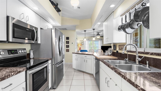 kitchen with sink, stainless steel appliances, light tile patterned floors, lofted ceiling, and white cabinets