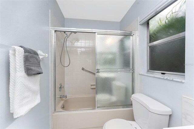 bathroom featuring toilet and shower / bath combination with glass door